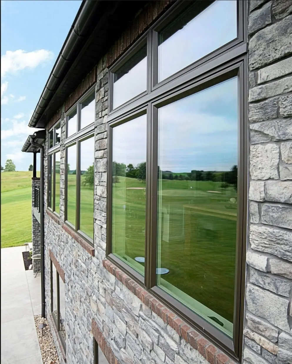Bronze-framed picture windows installed by Integrity on a natural stone home exterior.